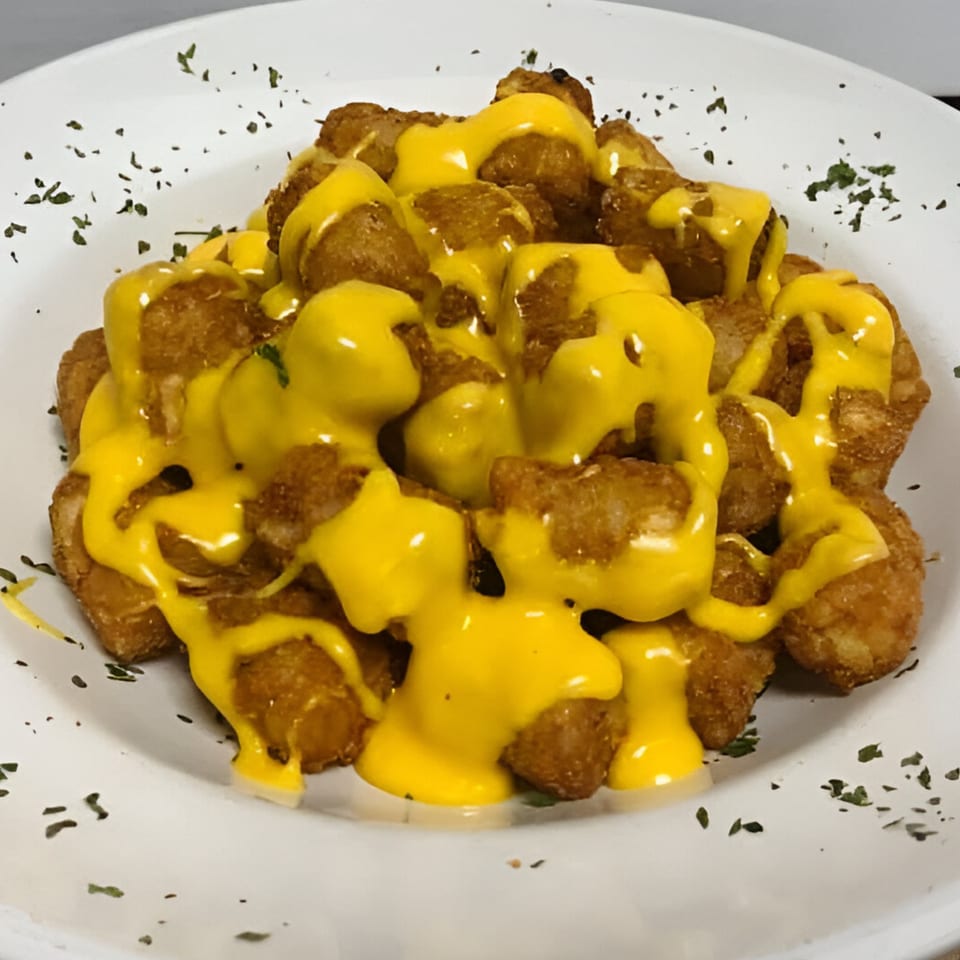 Golden-brown tater tots generously covered in melted yellow cheese and sprinkled with herbs.