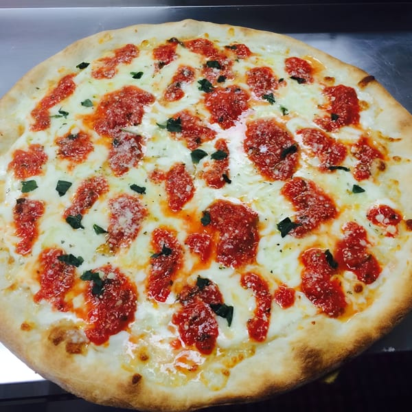 A freshly baked Sarappo's Pizza with melted mozzarella, red sauce, and basil on a metal surface.