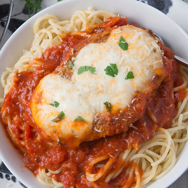 Chicken parmesan with melted cheese and parsley, served over spaghetti with red sauce in a white bowl.