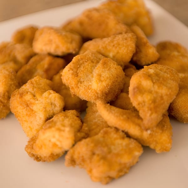 A close-up of a pile of golden-brown, breaded chicken nuggets on a white plate.