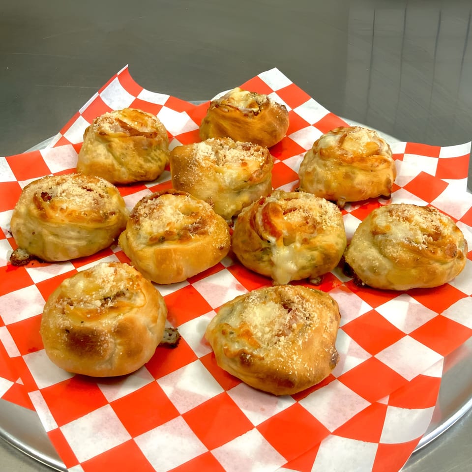 Ten golden-brown Sarappo's Pizza rolls with melted cheese and parmesan on red and white checkered paper.