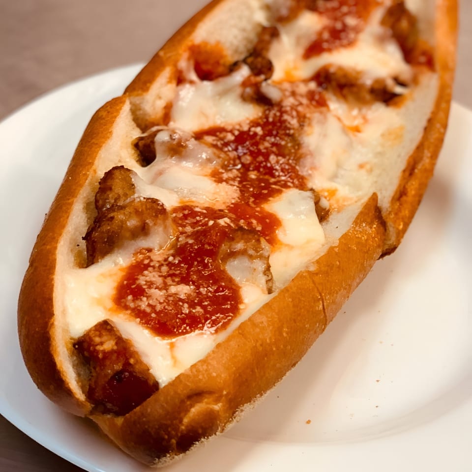A meatball sub sandwich with melted mozzarella cheese and marinara sauce on a white plate.